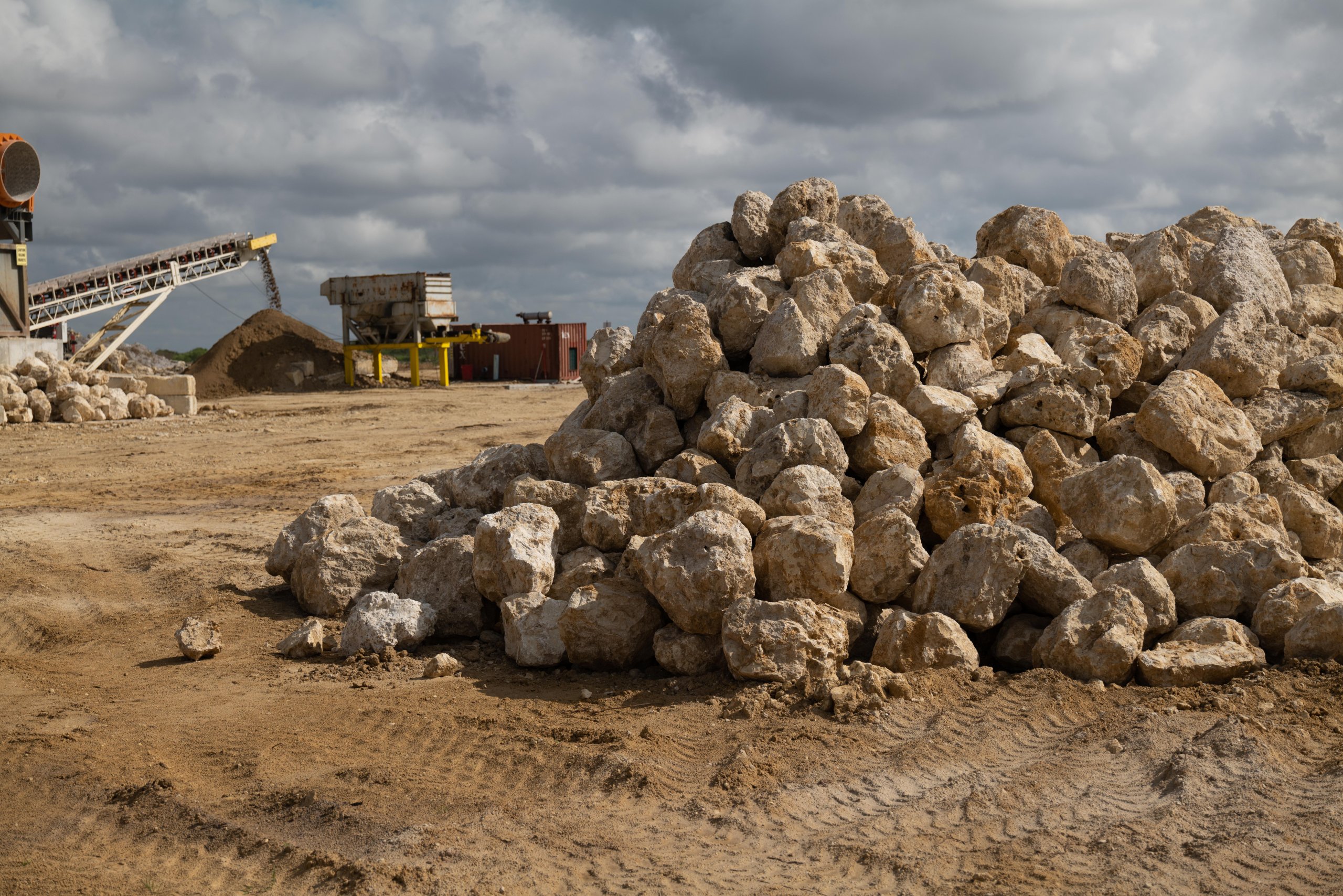 Stockpile of limerock rip rap boulders at Delta Aggregate's Immokalee, Florida facility with crushing equipment and conveyor visible in the background